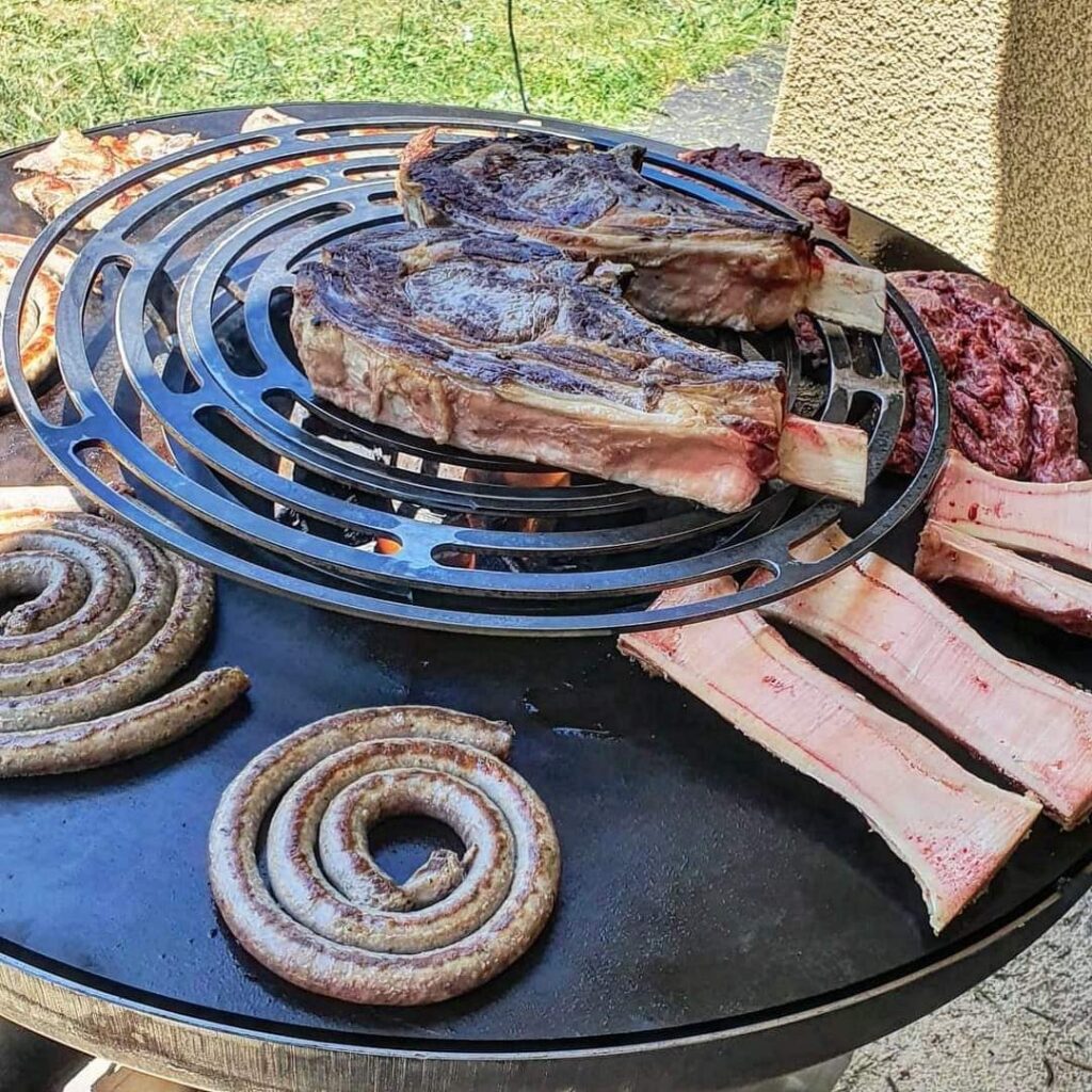 Côte de bœuf, saucisse en spirale et os à moelle sur la grille d'un braséro de 100