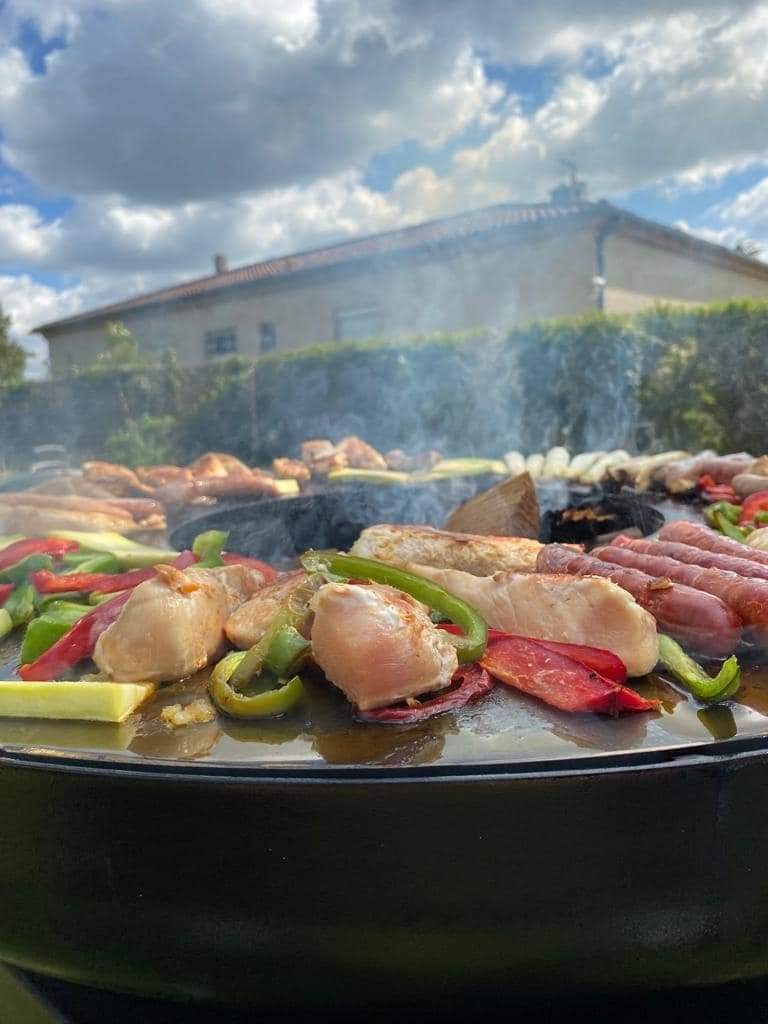 Poulet, poivrons et saucisses grillés sur le braséro rond de 100, maison et ciel nuageux derrière
