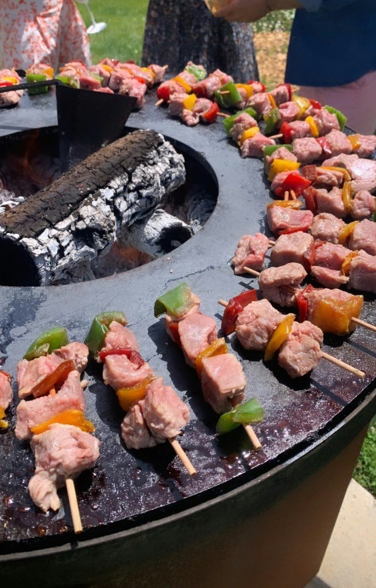 Brochettes de viande et de poivrons autour du foyer d'un braséro rond de 125