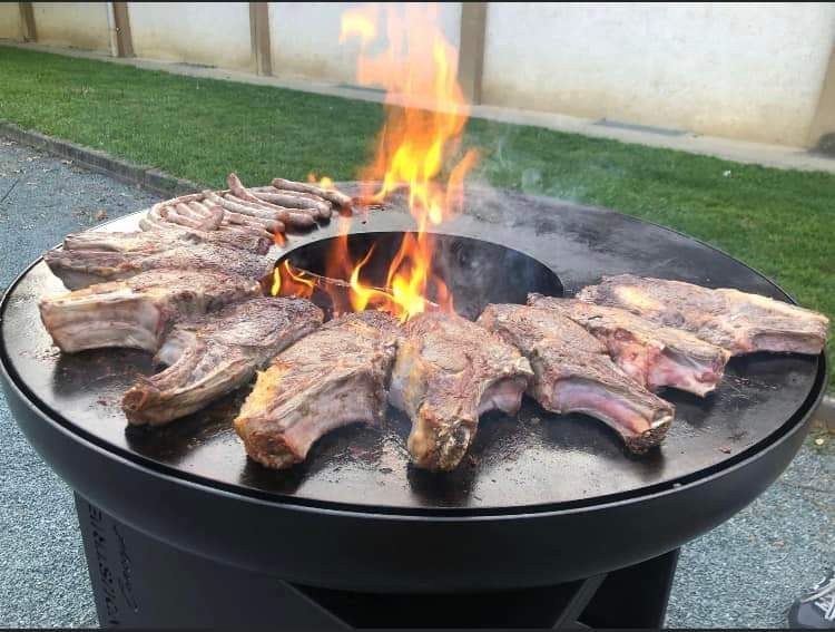 Côtes de bœuf en couronne autour du foyer enflammé d'un braséro rond de 125 sur meuble