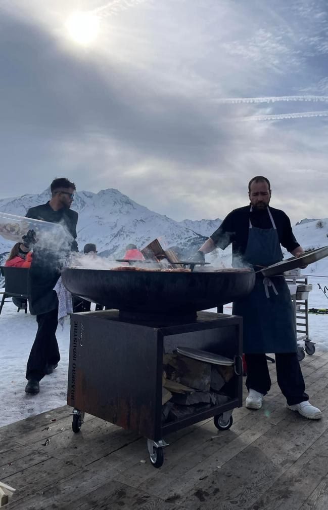 Cuisiniers devant un braséro de 125 sur meuble, paysage de montagne enneigée