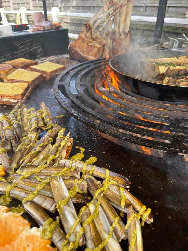 Couteaux de mer, pain grillé et poêle sur la plancha, côtes de bœuf suspendues au fond
