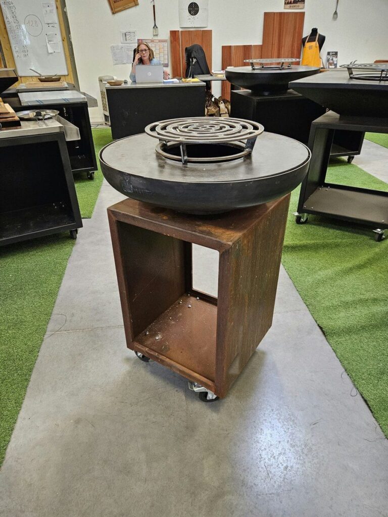 Braséro rond sur meuble en corten dans le showroom, autres braséros au fond