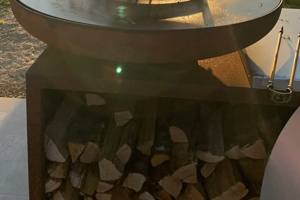 Braséro sur meuble avec réserve de bûches, au bord de l'eau au coucher du soleil