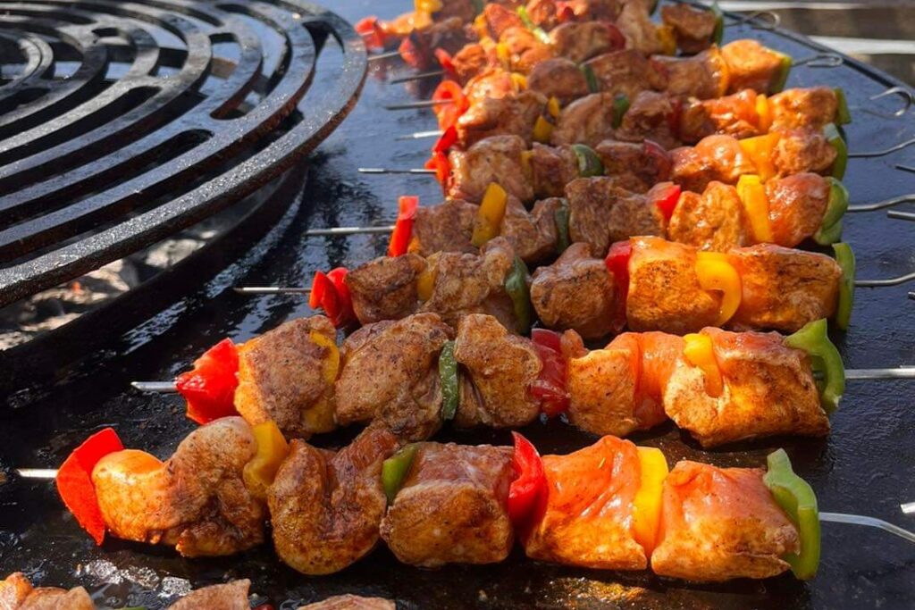 Brochettes de poulet et de poivrons alignées sur la plaque d'un braséro