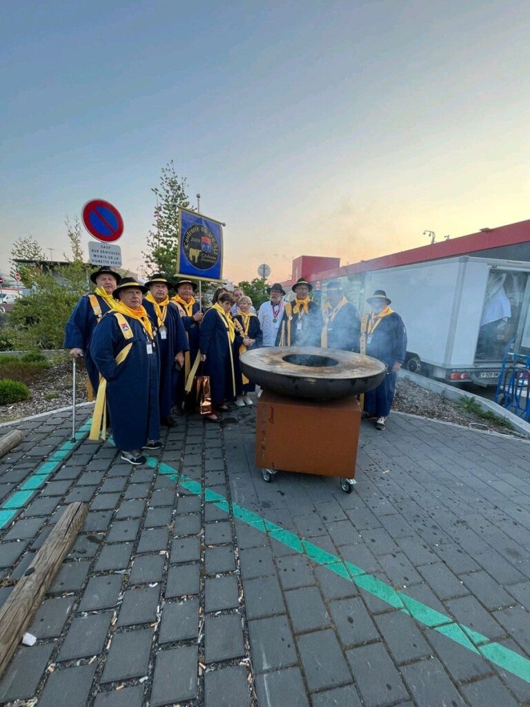 Confrérie en costume autour d'un braséro en acier corten sur une place, au crépuscule
