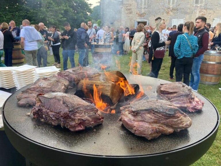 Côtes de bœuf autour d'une bûche enflammée sur un braséro de 150, public au fond