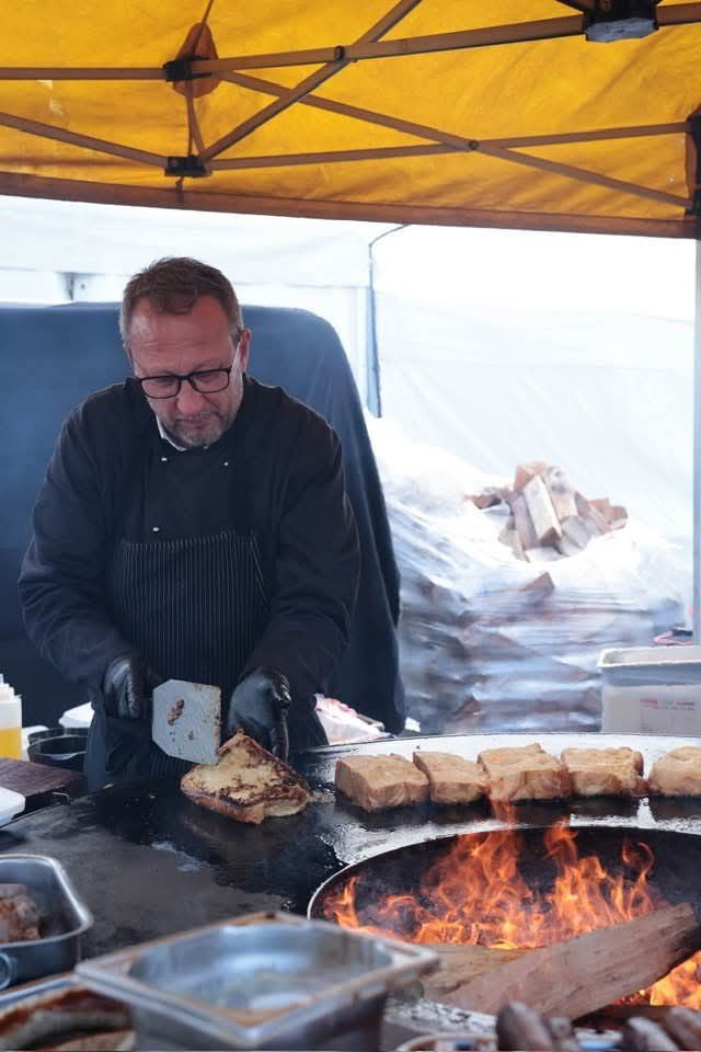 Cuisinier concentré devant un braséro en flammes, sous une tente jaune