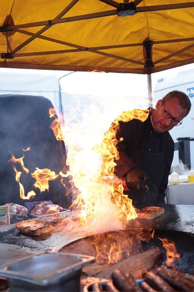 Cuisinier devant une grande flambée sur un braséro, sous une tente jaune