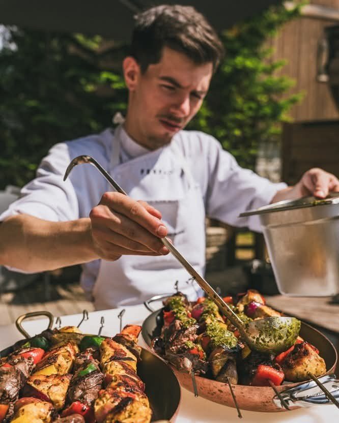 Cuisinier dressant un plat de brochettes et de légumes grillés