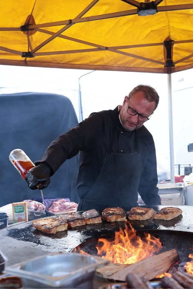 Cuisinier arrosant des côtes de viande sur un braséro, sous une tente jaune