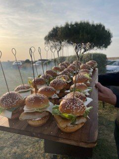 Mini burgers piqués sur une planche en bois au coucher du soleil