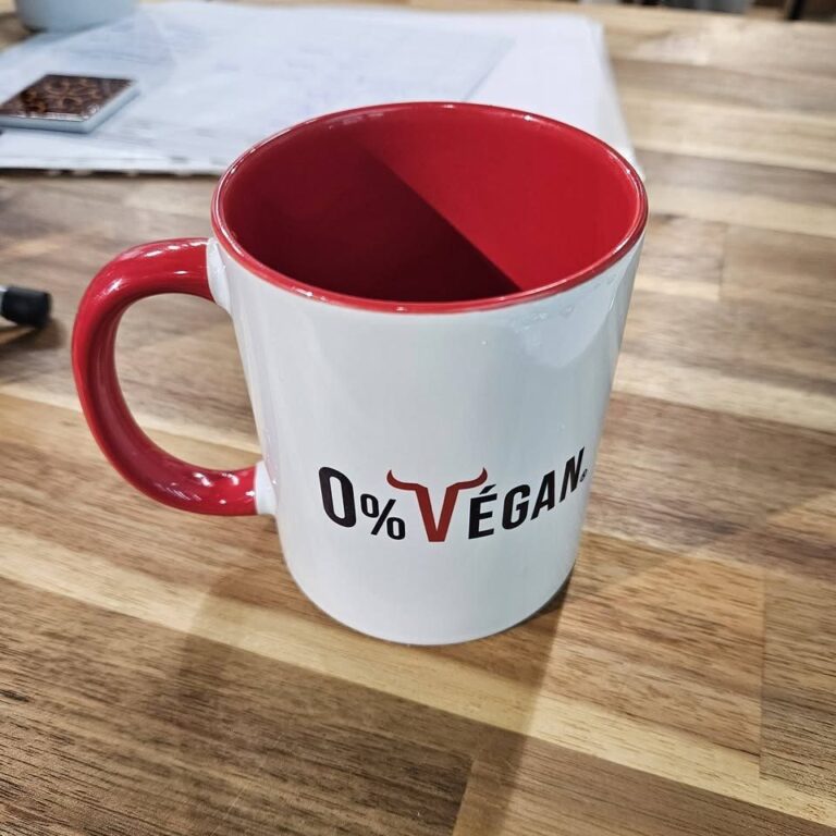 Mug 0% Végan à intérieur et anse rouges, posé sur un plan de travail en bois