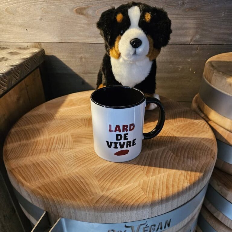 Mug « Lard de vivre » devant une peluche de chien, posé sur un billot de boucher