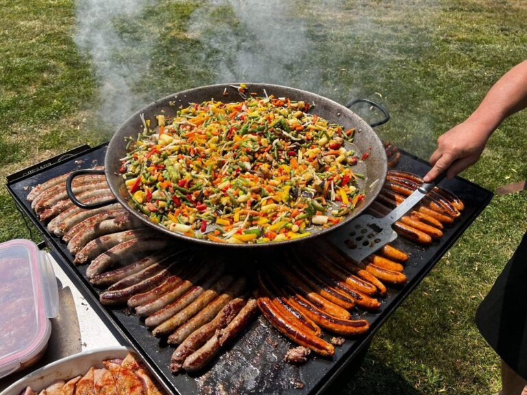 Paella de légumes posée sur des rangées de saucisses sur une grande plancha