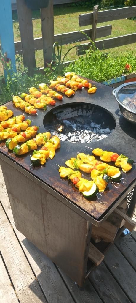 Plancha carrée sur meuble en acier, brochettes de poulet, légumes et braises