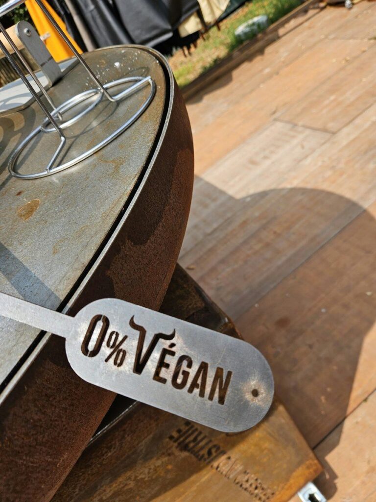 Plaque d'acier découpée 0% Végan posée devant un braséro en acier corten