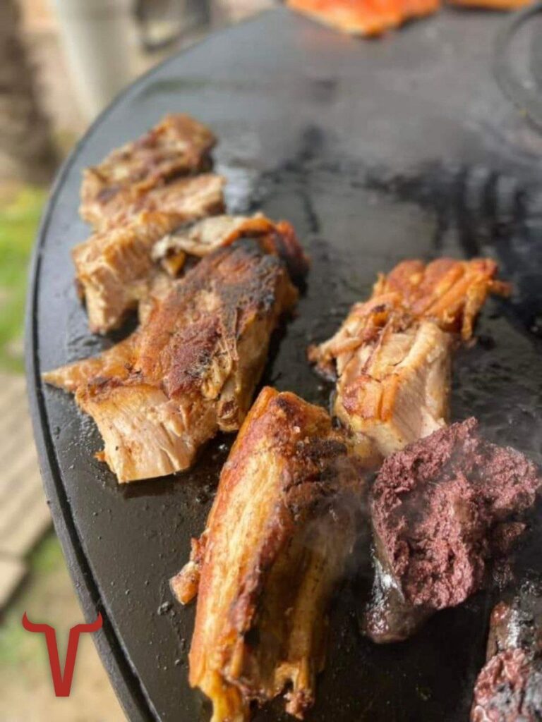 Gros plan sur de la poitrine de porc et du boudin noir qui grillent sur la plaque du braséro