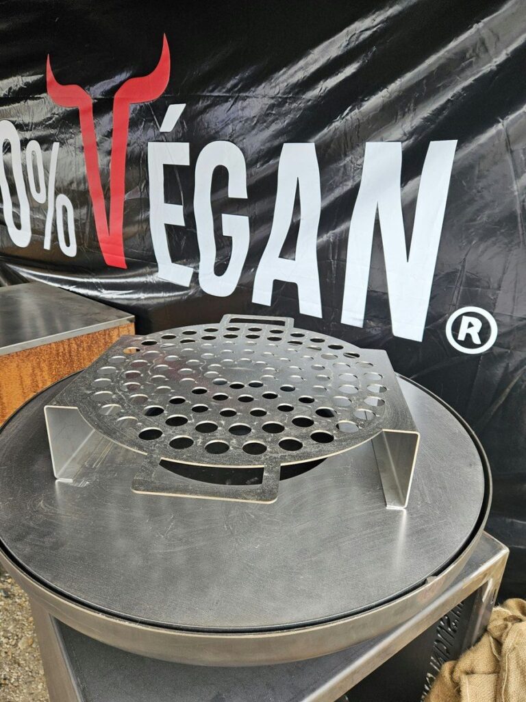 Grille à escargots en inox posée sur la plancha, banderole 0% Végan en fond