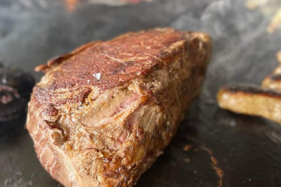 Pièce de bœuf saisie en gros plan sur la plaque d'un braséro, grille en spirale derrière
