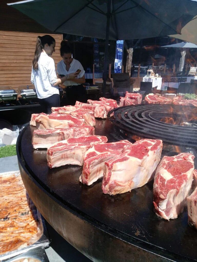 Côtes de bœuf alignées sur la plancha d'un braséro monté sur remorque, public derrière