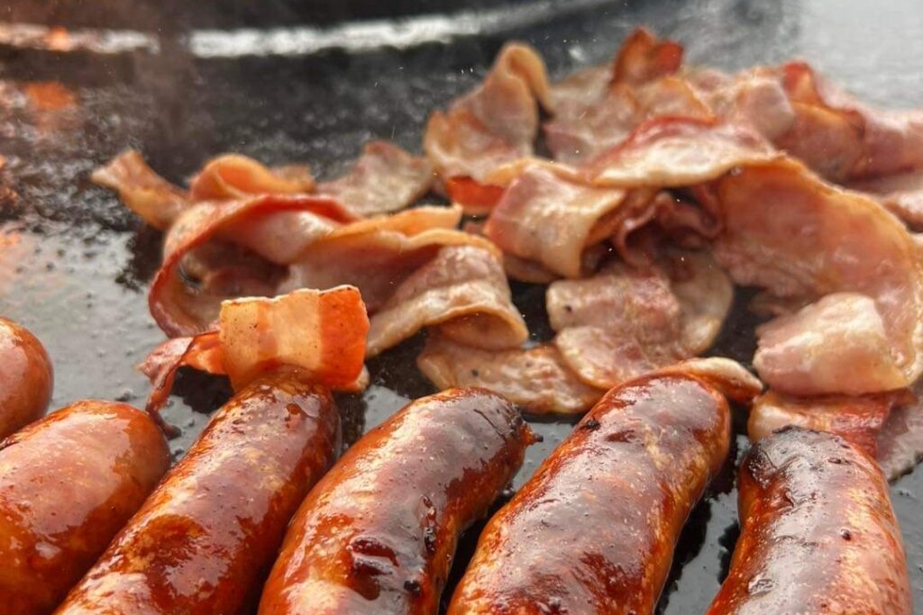 Chipolatas et lard grillés sur la plaque d'un braséro