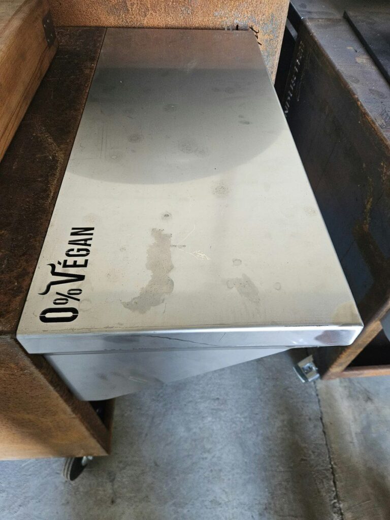 Tablette inox posée sur un meuble de braséro, logo 0% Végan noir dans l'angle