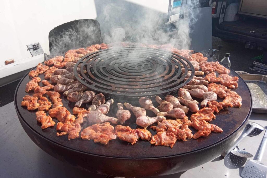 Pilons et morceaux de poulet marinés en couronne autour de la grille ronde de la plaque, un peu de fumée au-dessus